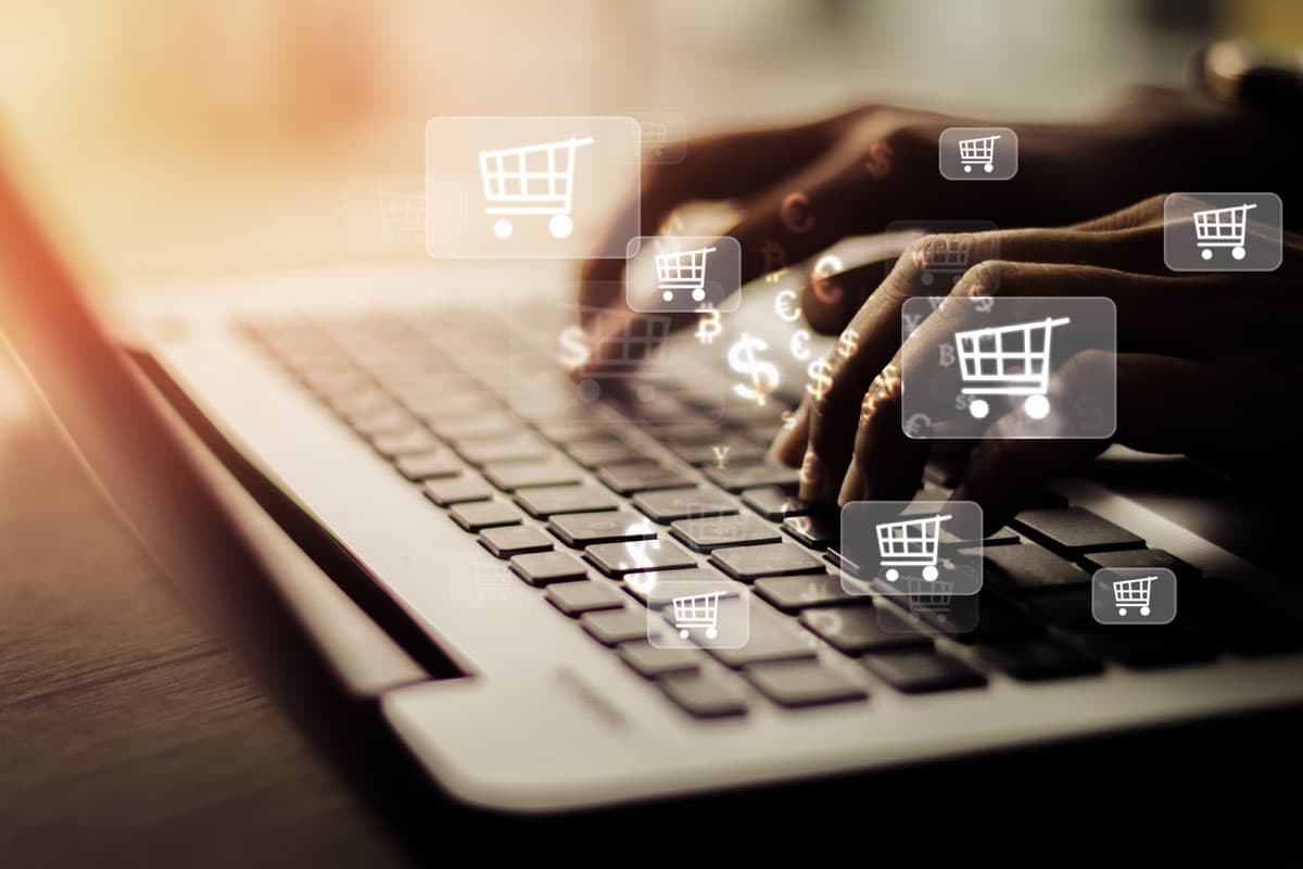 Persona escribiendo en laptop con íconos de carrito de compra y símbolos de moneda, representando el crecimiento de ventas en un ecommerce
